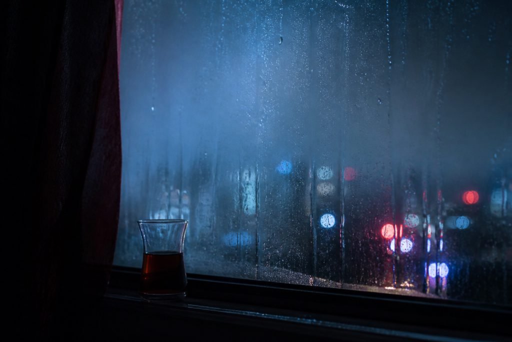Yağmurlu pencere önünde çay bardağı ve gece ışıkları